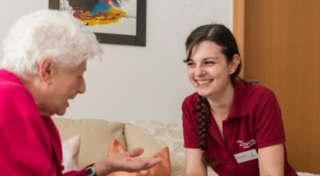 Pflegerin und ältere Dame unterhalten sich auf dem Sofa sitzend